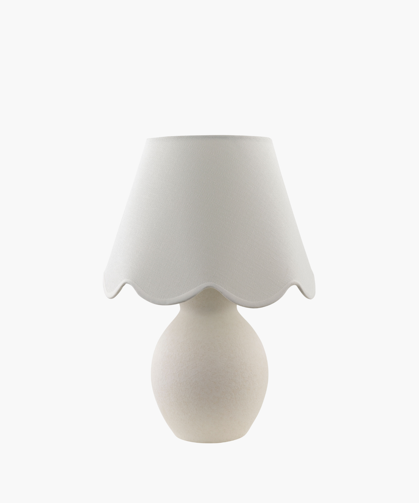 A cream-colored table lamp with a rounded base and a scalloped fabric shade, conveying a cozy and elegant feel. The design is minimalist and classic.