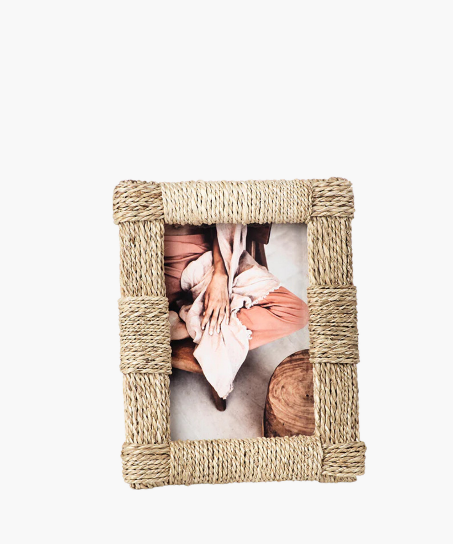 A rustic, woven rope frame with a picture of a person in with pink pants sits on the floor, with legs bent and arms resting on knees.