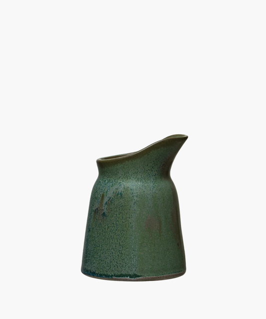 Green glazed ceramic creamer with a smooth, speckled texture and a curved spout. The design is modern and minimalist, evoking calm and simplicity.