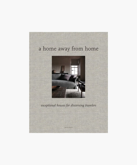 A cover of "A Home Away from Home" book; showcases a cozy, elegant living room with a gray sofa and large window, evoking warmth and sophistication.