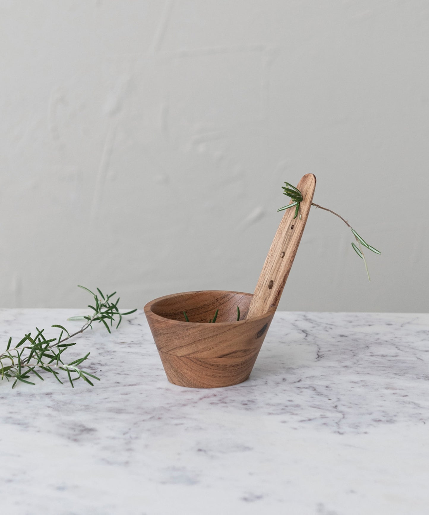 A natural Acacia wood herb stripper featuring a cylindrical bowl and a paddle-like handle with holes. The wood grain is prominent, conveying a rustic, hand-crafted feel.