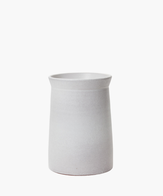 A minimalist, cylindrical white ceramic vase with a slightly flared rim against a plain white background, conveying simplicity and elegance.