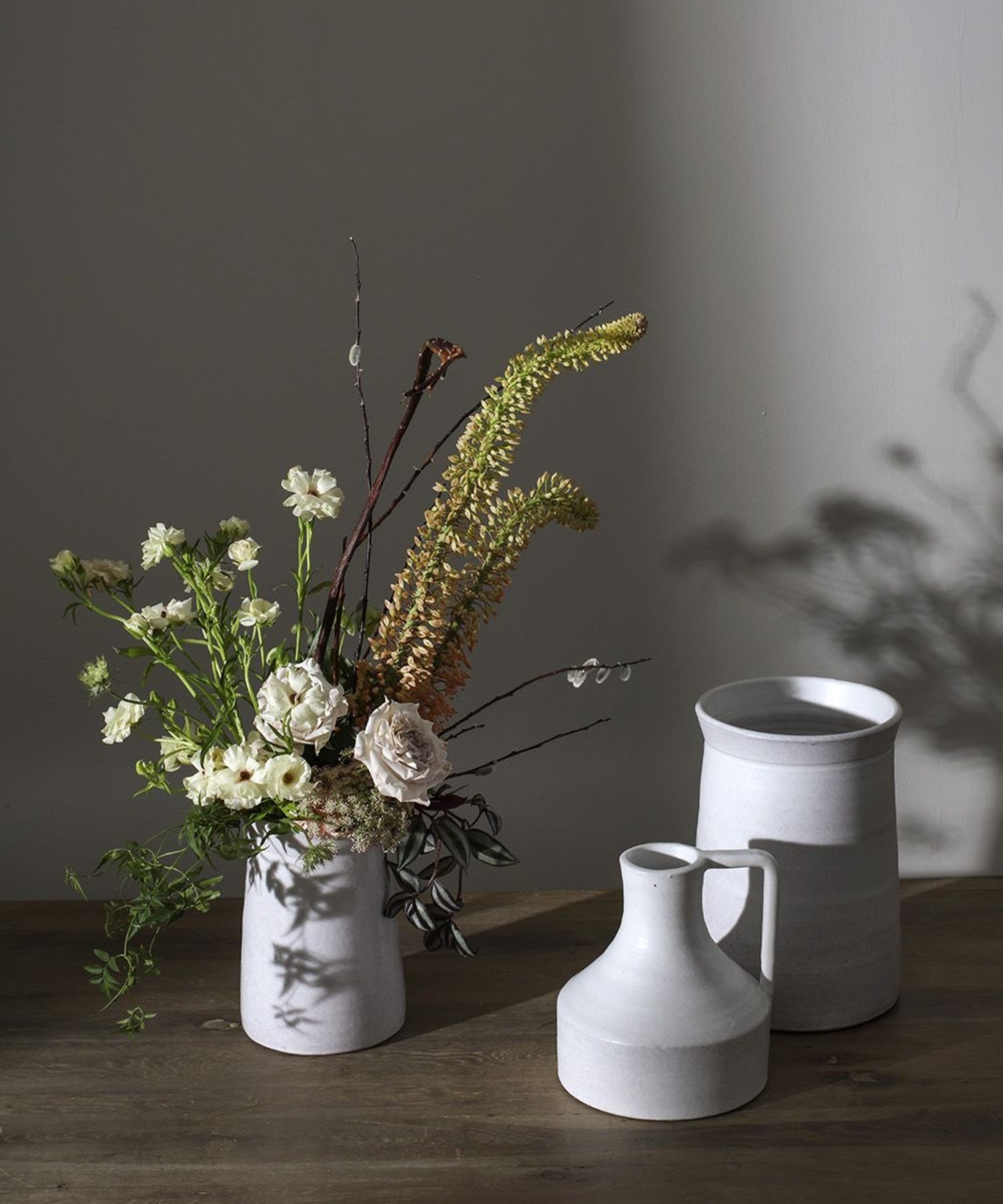 Three minimalist terracotta vases with a white matte finish of varying heights and shapes, conveying simplicity and elegance styled with a neutral floral arrangement. 