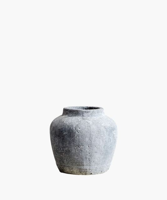 A rustic, gray stone vase with a round body and narrow neck against a white background. The textured surface and simple design suggest an ancient, timeless quality.