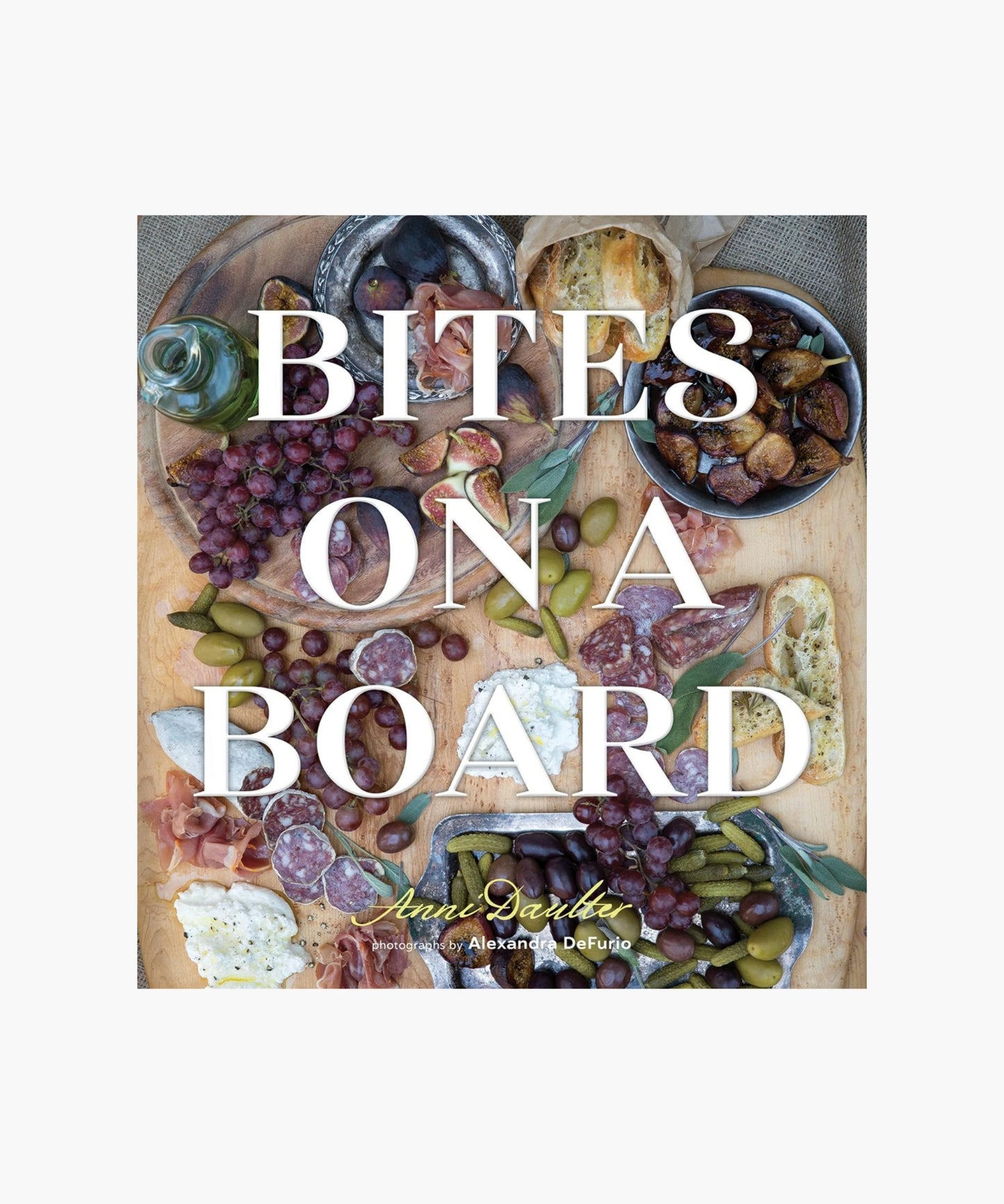 The cover of the book "Bites on a Board" by Anni Dauter featuring a charcuterie board with grapes, olives, figs, cured meats, bread, and cheese. The text "Bites on a Board" overlays the image, evoking a rustic, savory feel.