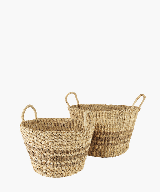 Woven seagrass baskets in a natural and brown tone with two loop handles and subtle striped accents in 2 sizes. The baskets have a simple, rustic design, featuring a slightly flared rim. 