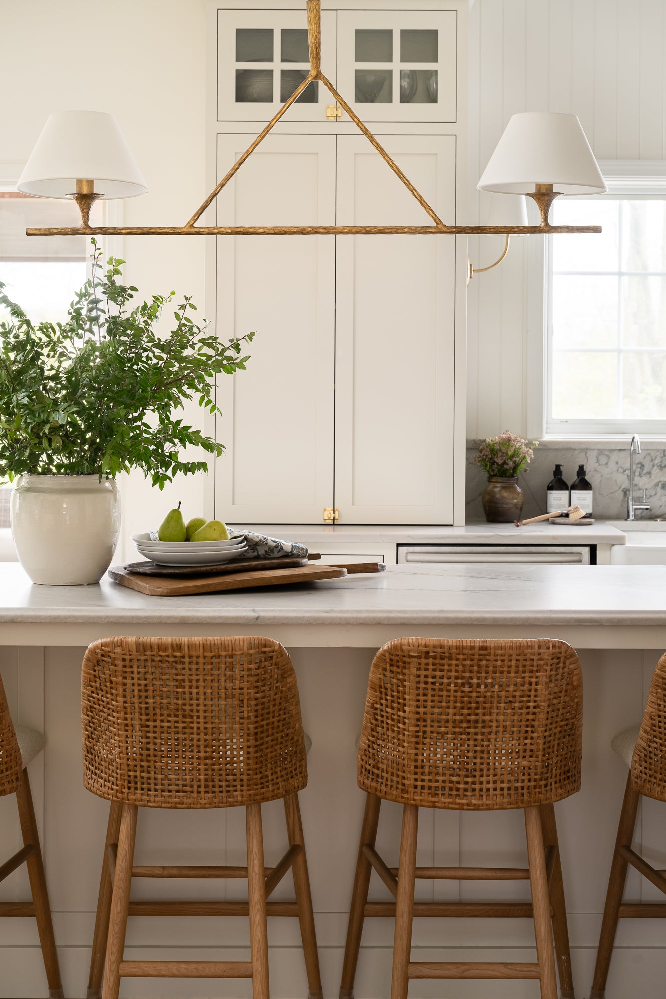 White ceramic pot with two small handles on each side styled on a kitchen counter with greenery. The smooth, glossy surface and wide opening give a simple, elegant appearance.