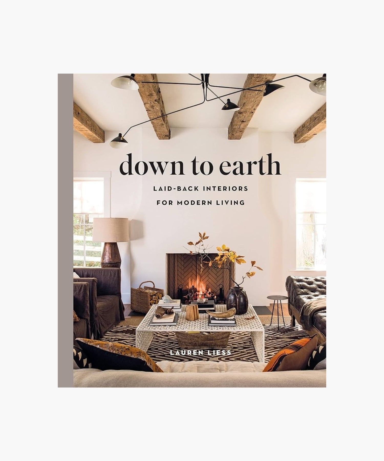 The cover of the book "Down to Earth" by Lauren Liess features a living room with a cozy fireplace, rustic wooden beams, a patterned rug, and modern furniture. The atmosphere is warm and inviting.