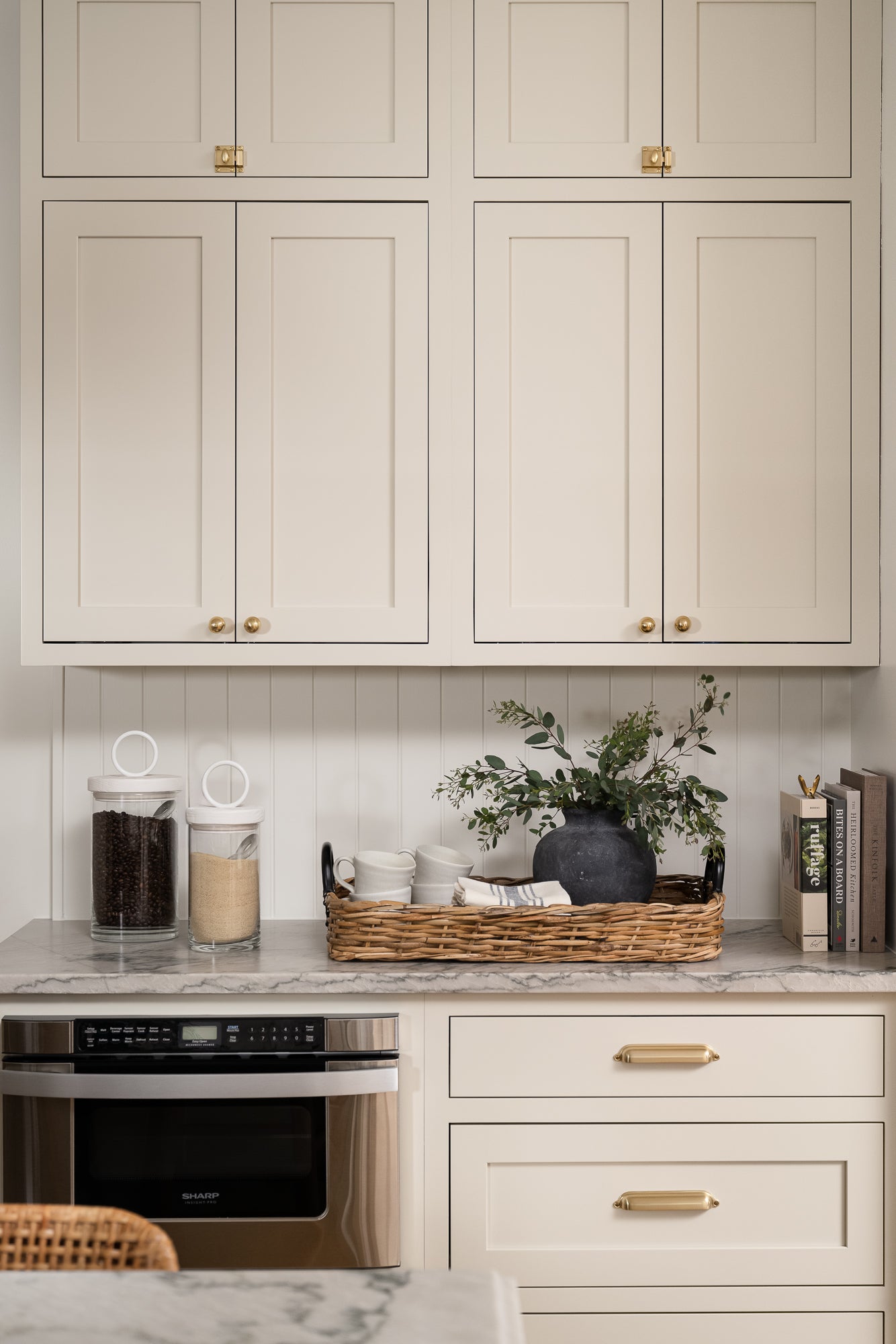 A large, round, weathered gray clay vase with a narrow neck styled with greenery on a kitchen counter. 