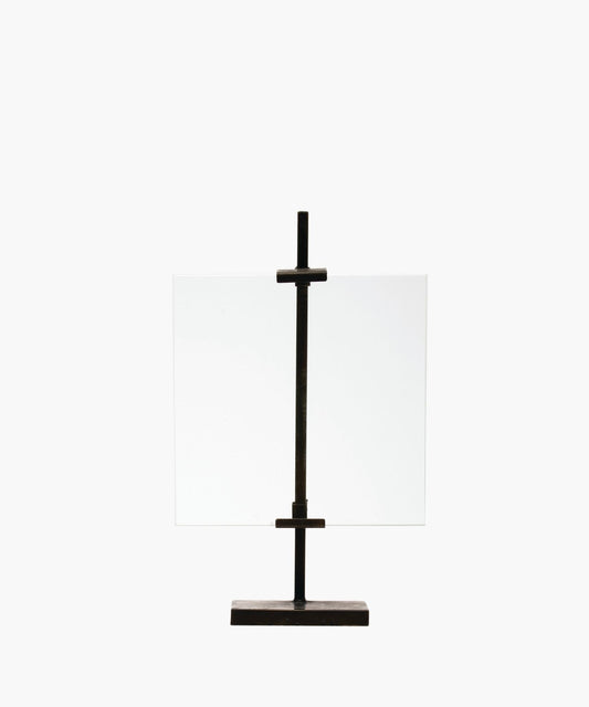 A minimalist black metal display stand with a vertical metal clamps holds a clear, rectangular glass sheet. The simple design exudes an industrial, modern feel.