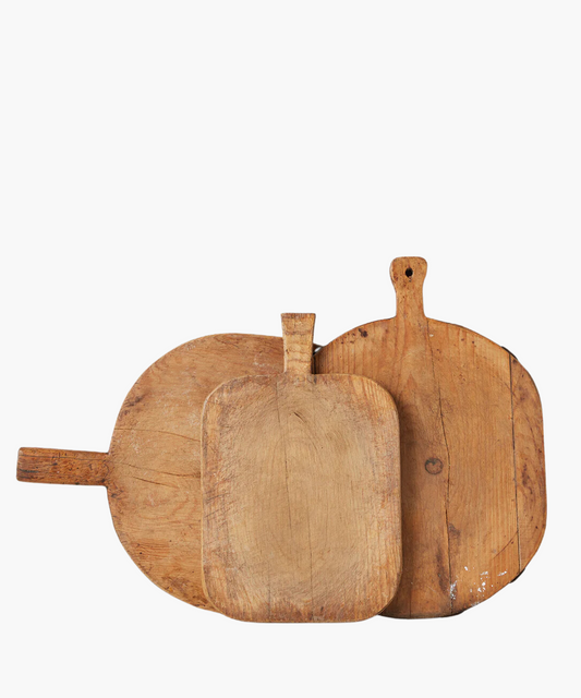 Three rustic, wooden cutting boards of varying shapes and sizes overlap. Their worn texture suggests frequent use, conveying a homely, vintage feel.