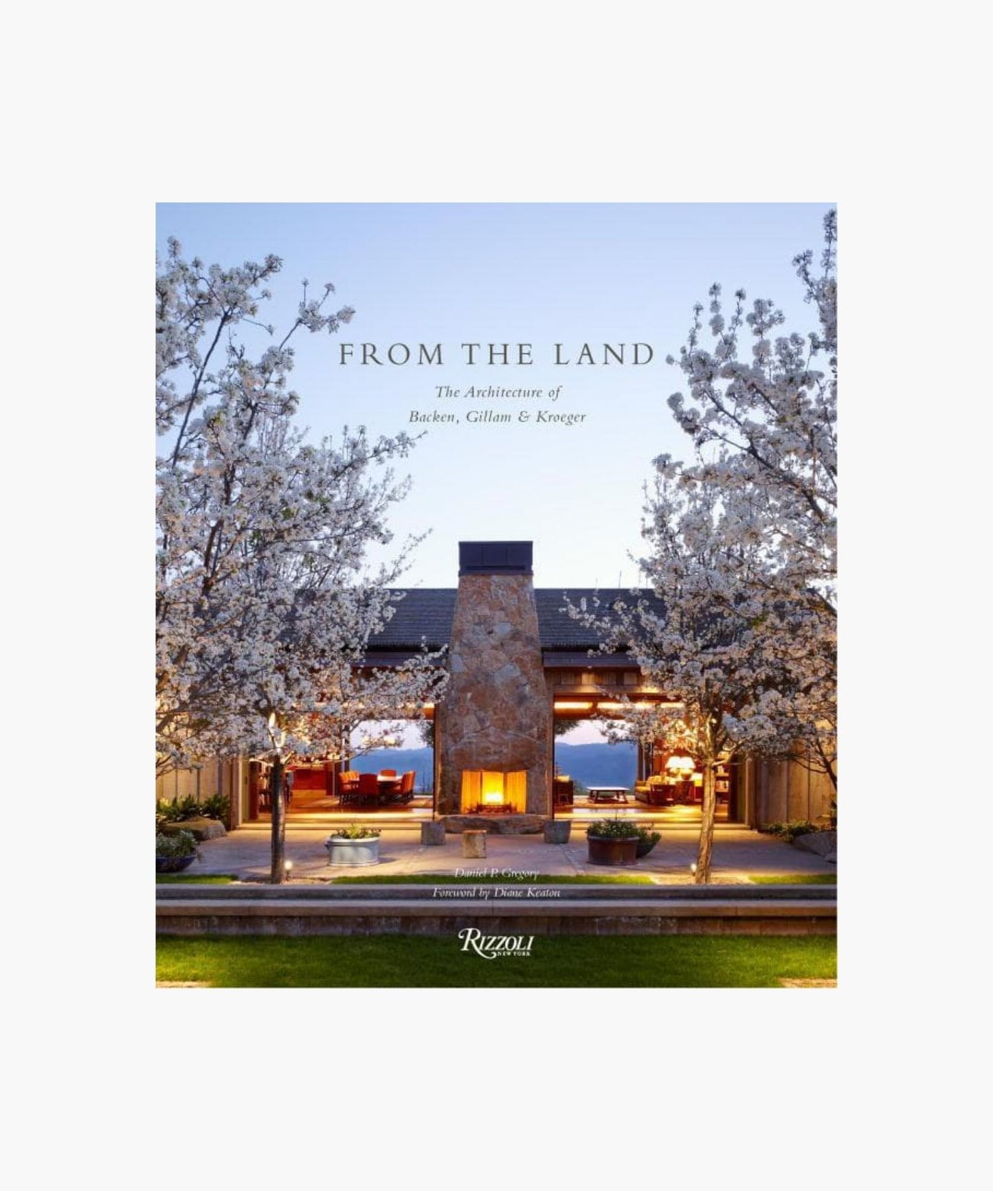 Cover of the book "From The Land" features an outdoor stone fireplace flanked by blossoming trees, with a warmly lit interior visible through large windows. Evening sky backdrop; peaceful ambiance.