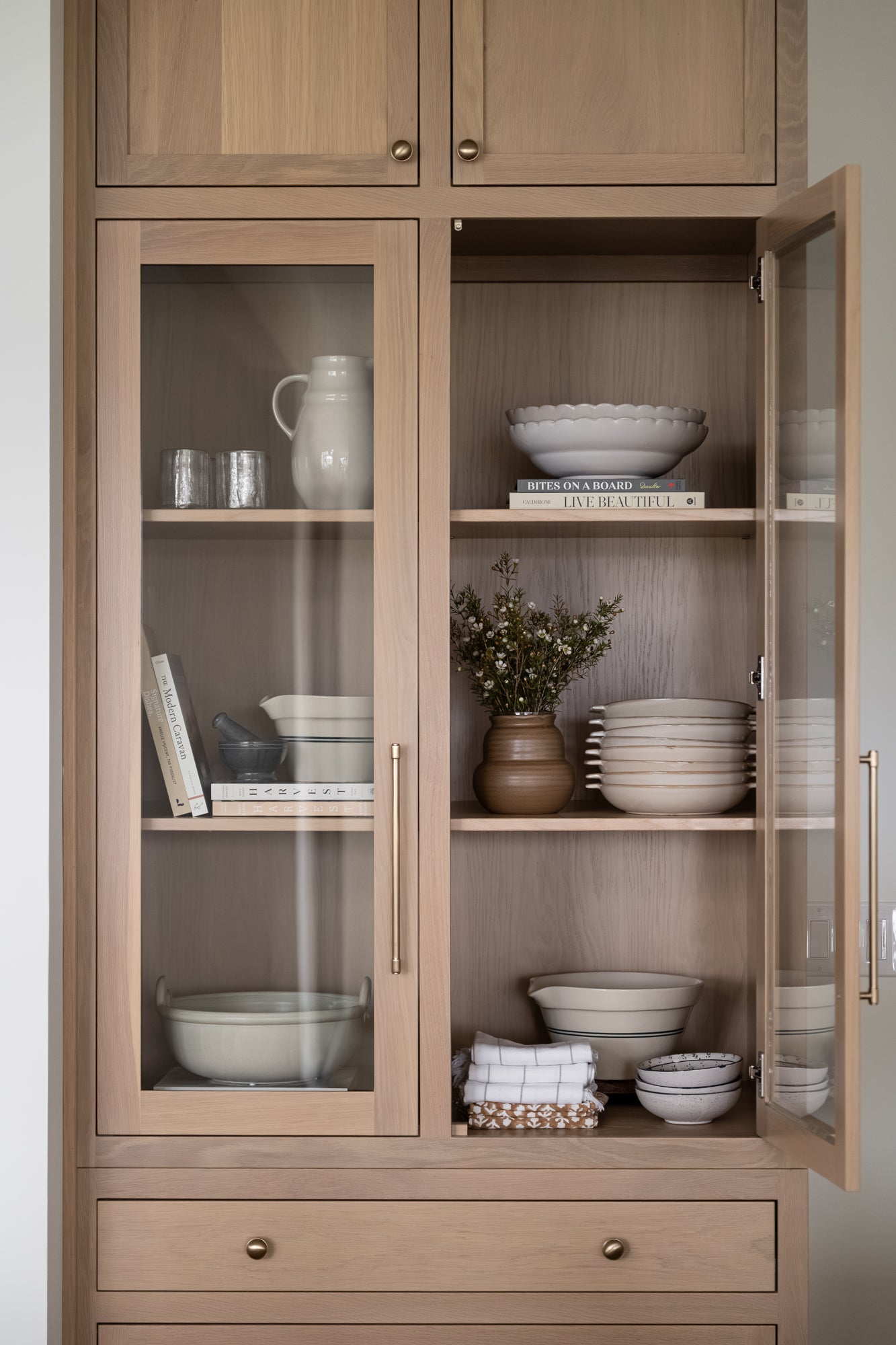 Green bowl with a scalloped edge styled on a shelf with books, bowls, glassware, and a pitcher. 