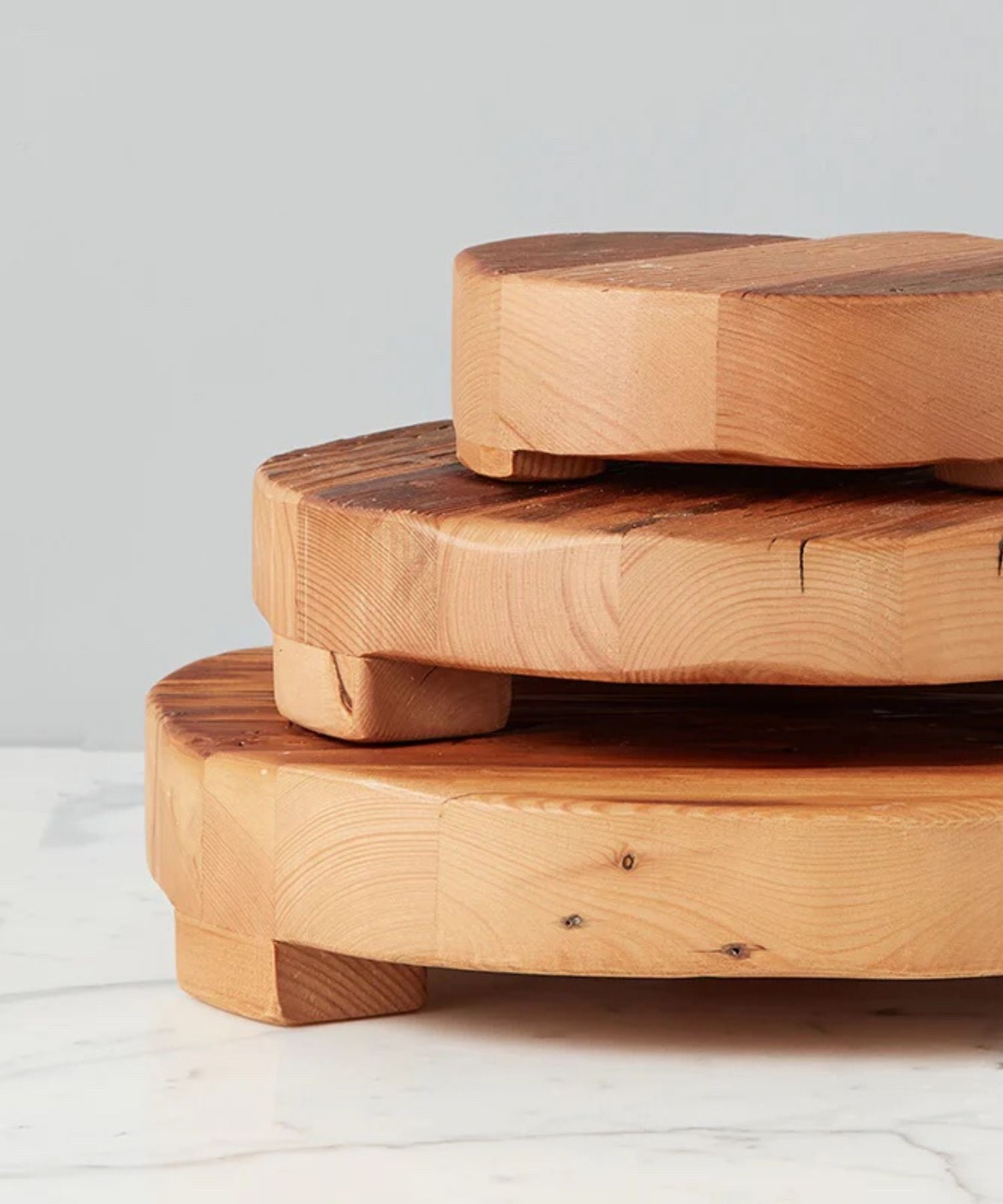 Round wooden pedestal or trivet made of smooth, natural wood with subtle grain patterns, supported by small rounded legs in 2 sizes. Conveys rustic and minimalist elegance.