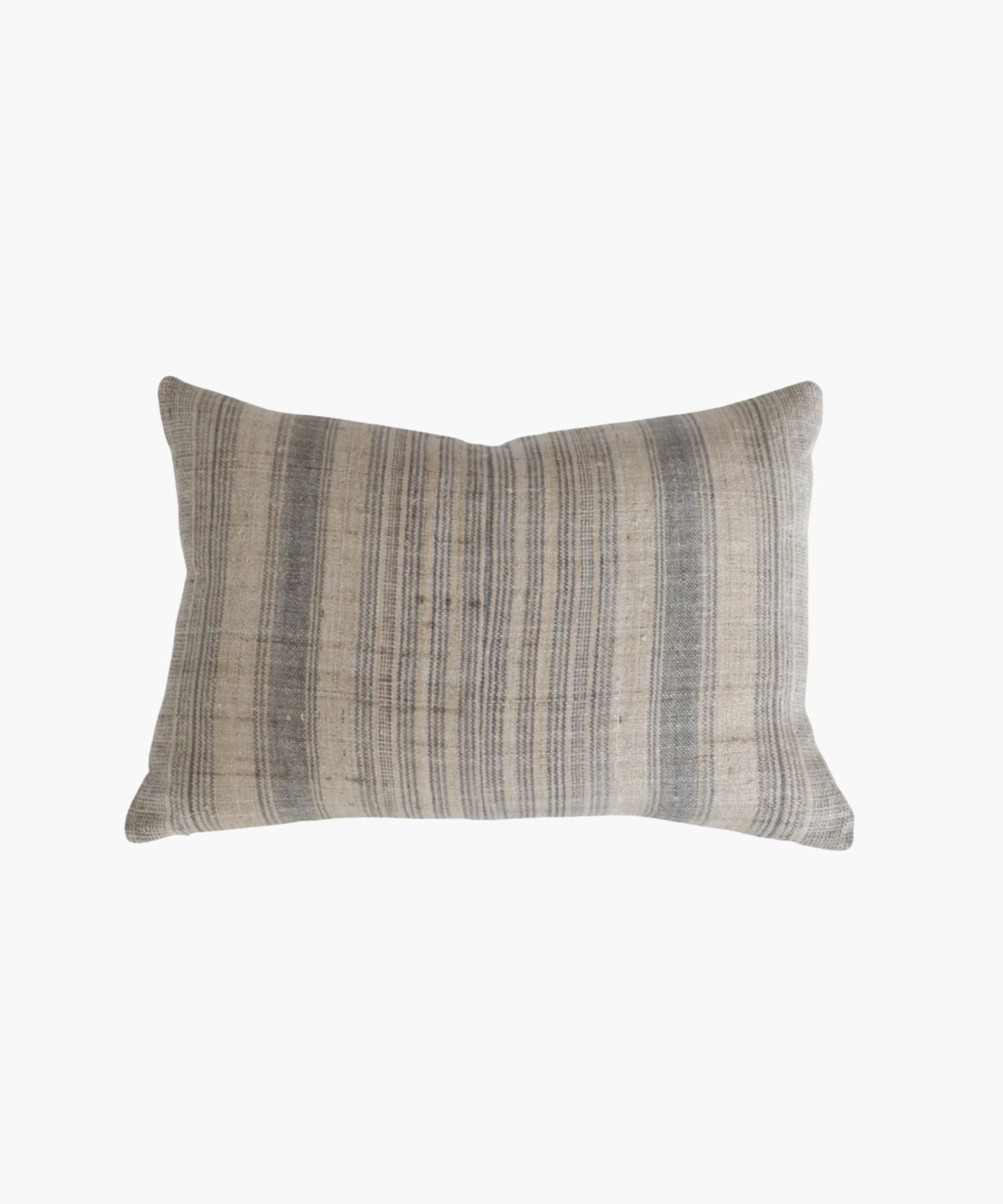 A rectangular or lumbar pillow cover with a neutral hemp background features vertical grey and blue stripes. The texture appears soft and slightly textured, conveying a cozy and rustic feel.