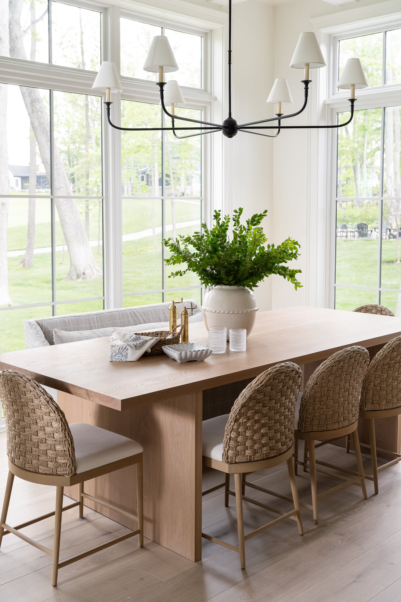 A white ceramic pot with a glossy surface and rounded shape. It features a decorative band with a loop design near the top styled on a kitchen table with greenery. 