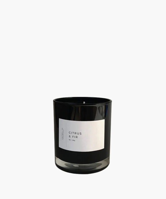 A white candle in a glass jar with a minimalist label reading "Citrus & Fir." The design conveys a clean, calming aesthetic.