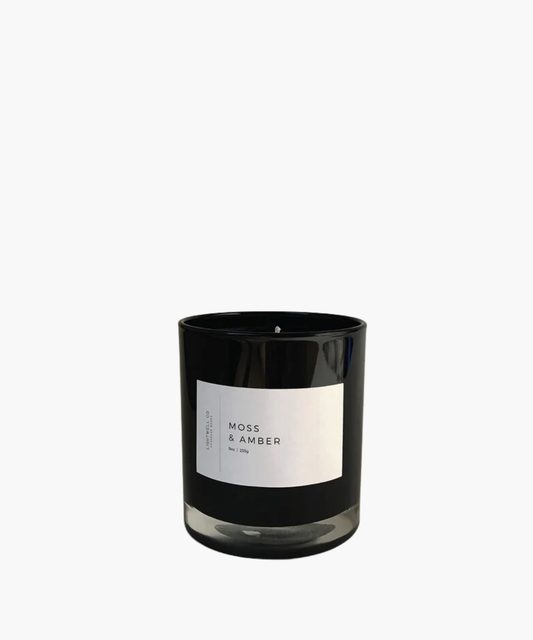 Black candle jar labeled "Moss & Amber" by Lightwell Co, 9 oz. Simple, elegant, and modern design, conveying a calm and sophisticated mood.