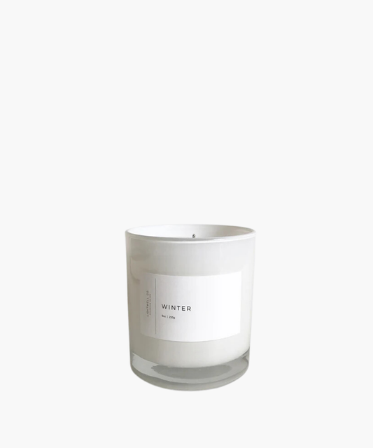 White candle in a transparent glass jar, labeled "Winter" with a minimalist design. Evokes a clean, calming aesthetic, suggesting a cozy seasonal ambiance.