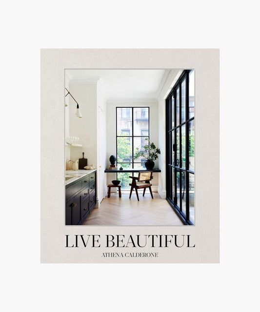 The cover of the book "Live Beautiful" by Athena Calderone features a stylish interior design with large windows, minimalistic furniture, and natural light. The tone is serene and elegant.