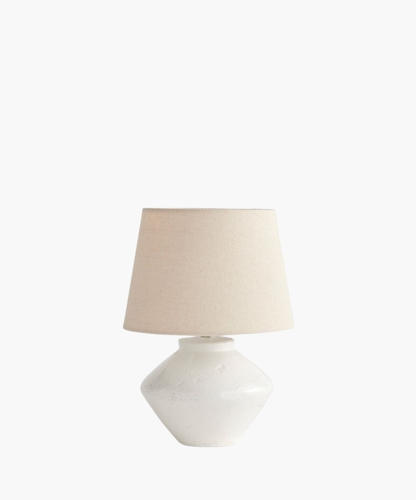 A cream table lamp with a textured, wide ceramic base and a simple fabric shade. The lamp's minimalist design evokes a calm and neutral tone.