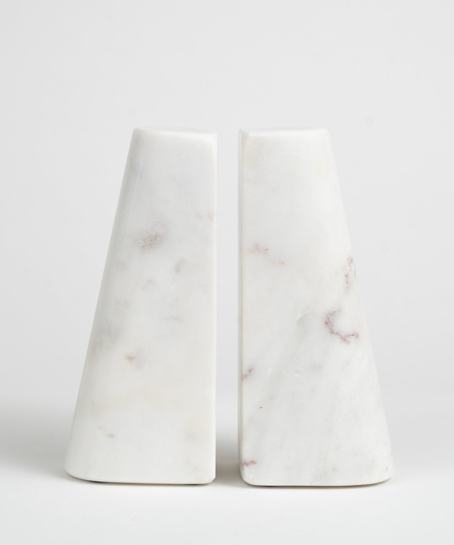 Two white marble bookends with a smooth, conical shape, each featuring subtle brown and gray veining. They appear minimalist and elegant.