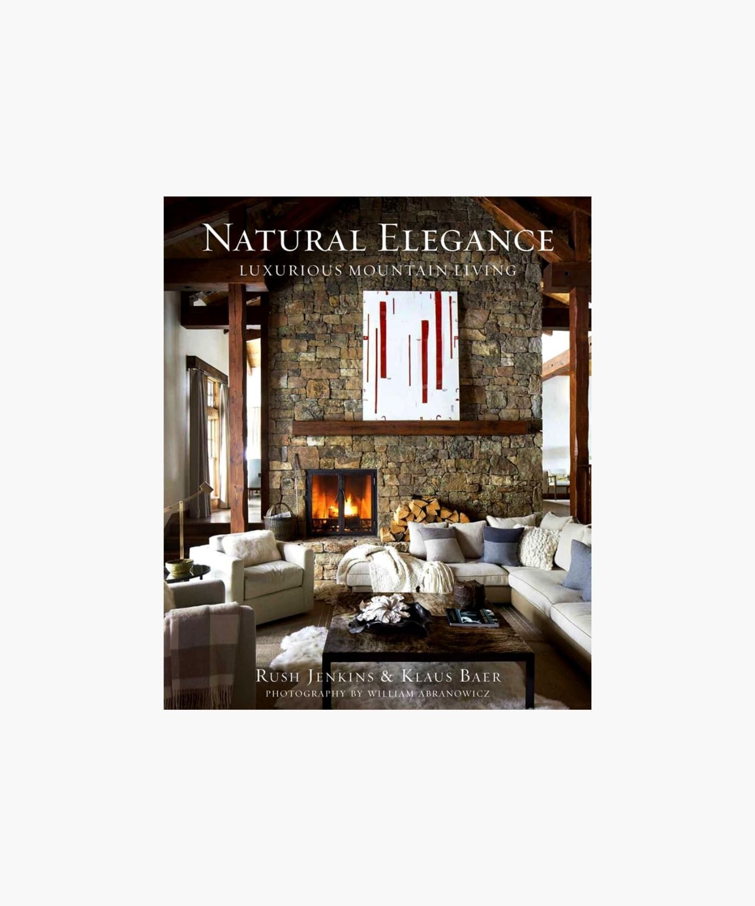 The cover of the book "Natural Elegance: Luxurious Mountain Living" by Rush Jenkins and Klaus Baer features a cozy, elegant living room features a stone fireplace, modern art, and a plush sectional. Warm tones and natural light create a welcoming, luxurious atmosphere.