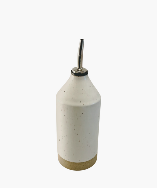 A ceramic olive oil dispenser with a speckled white body and a tan base. It features a metal spout and minimalist design.