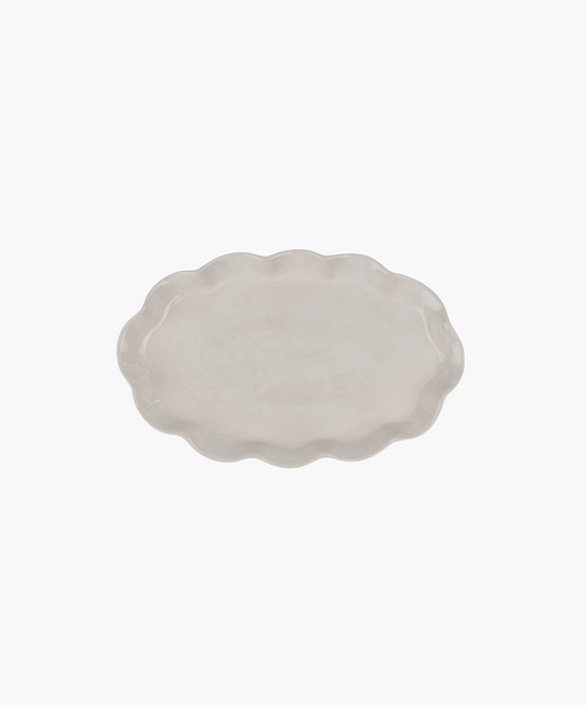 An oval, ceramic platter with a wavy, scalloped edge in a light cream color. The minimalist design conveys simplicity and elegance.