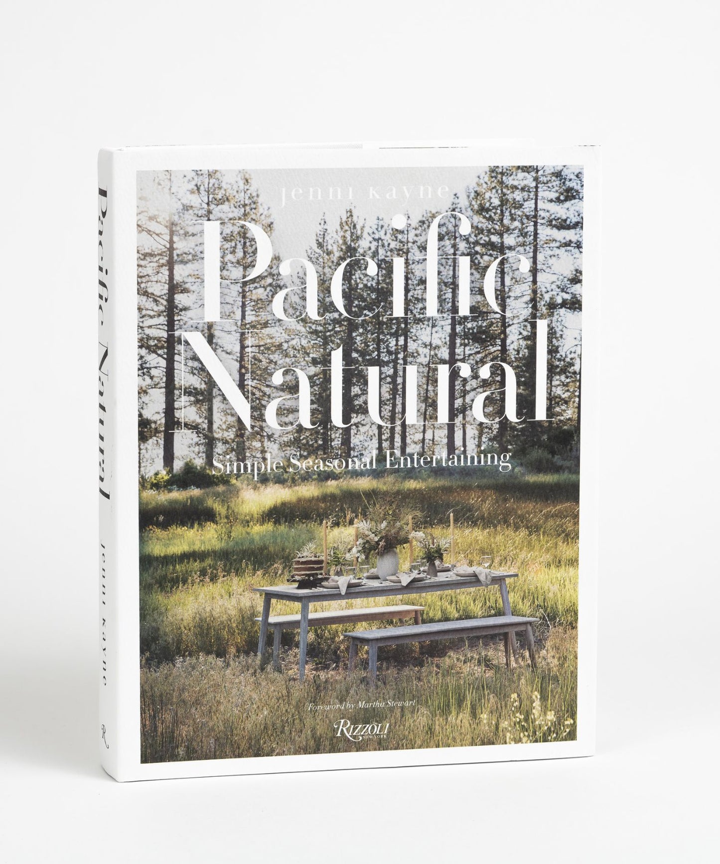 The cover of the book "Pacific Natural" by Jenni Kayne featuring a serene outdoor picnic scene with a rustic table set in a sunlit forest, conveying tranquility and elegance.