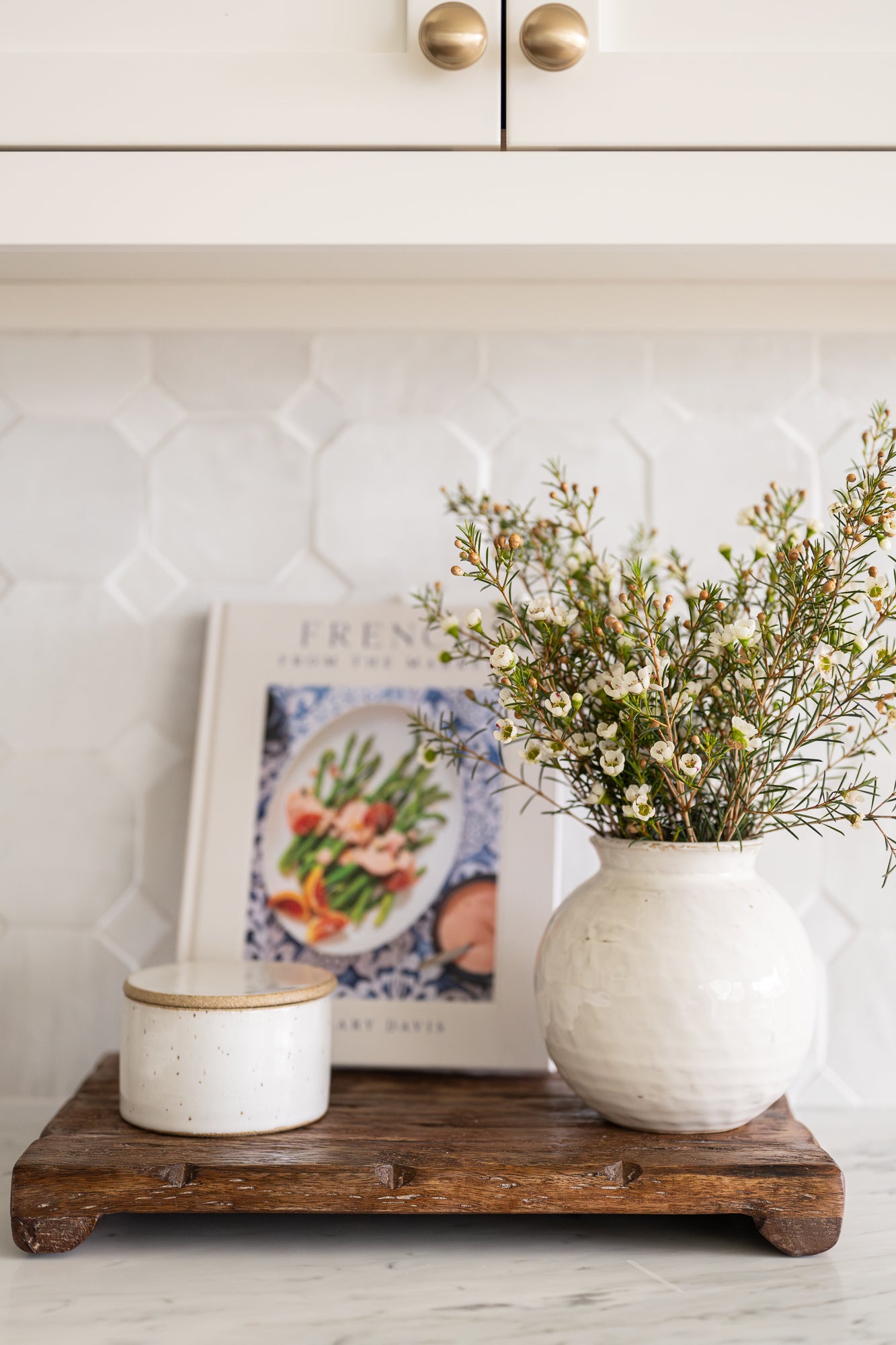 Ceramic round-bellied pot with a white glaze styled with salt cellar and cookbook. 