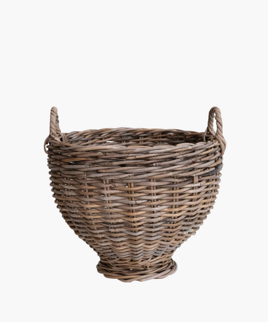 A handwoven round rattan footed basket with two small handles, featuring a natural brown tone. The basket has a rustic, handcrafted appearance, conveying a traditional and homely feel.