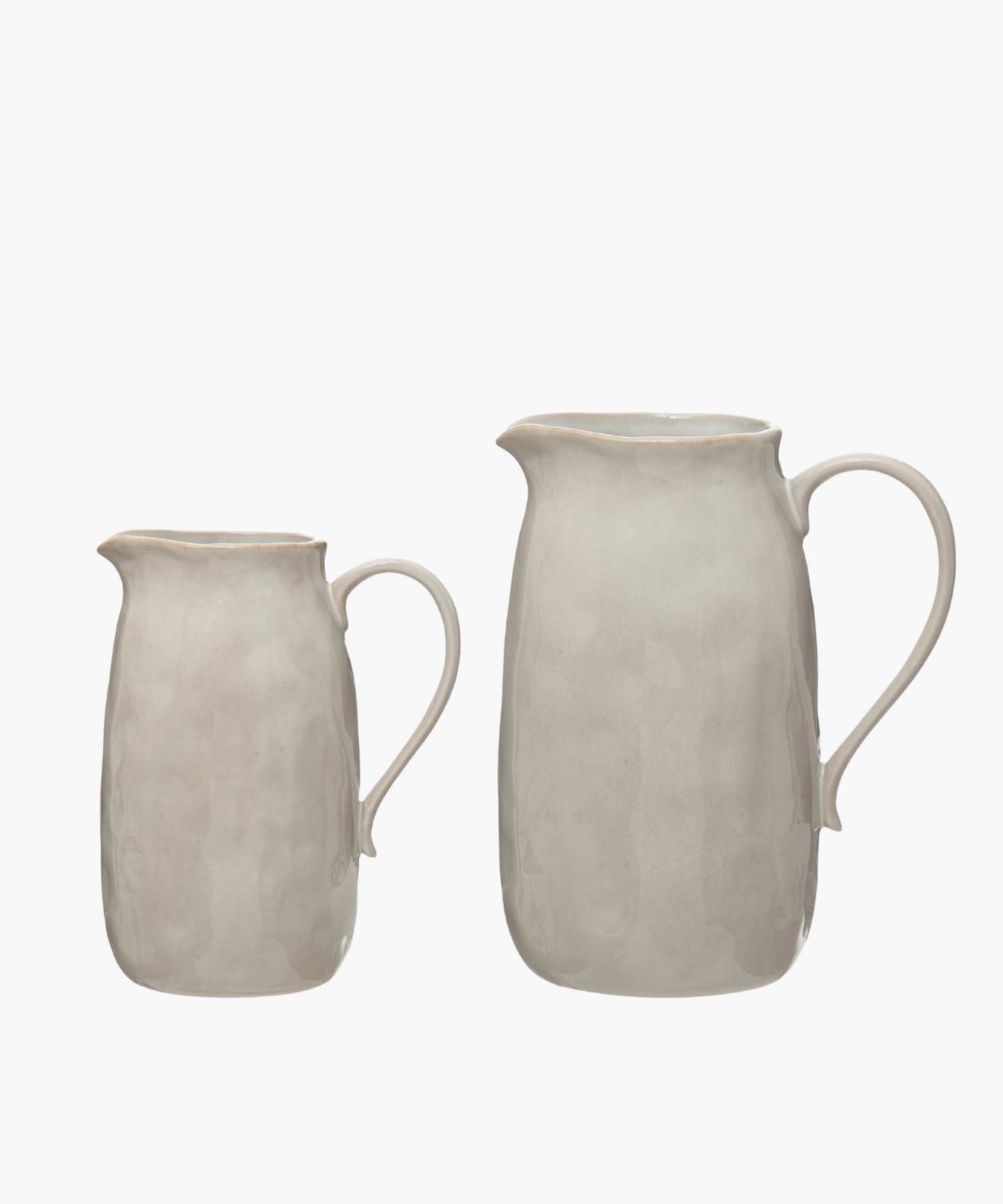 Two simple, elegant beige ceramic pitchers in various sizes with a smooth curved handle and a subtly textured surface, evoking a minimalist and classic design.