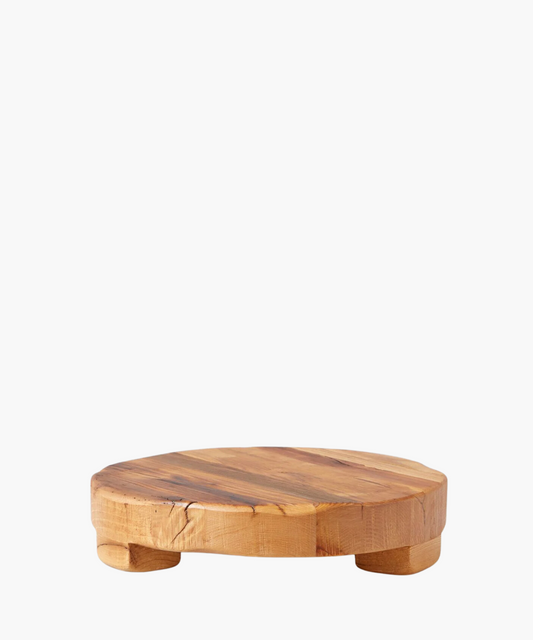 Round wooden pedestal or trivet made of smooth, natural wood with subtle grain patterns, supported by small rounded legs. Conveys rustic and minimalist elegance.