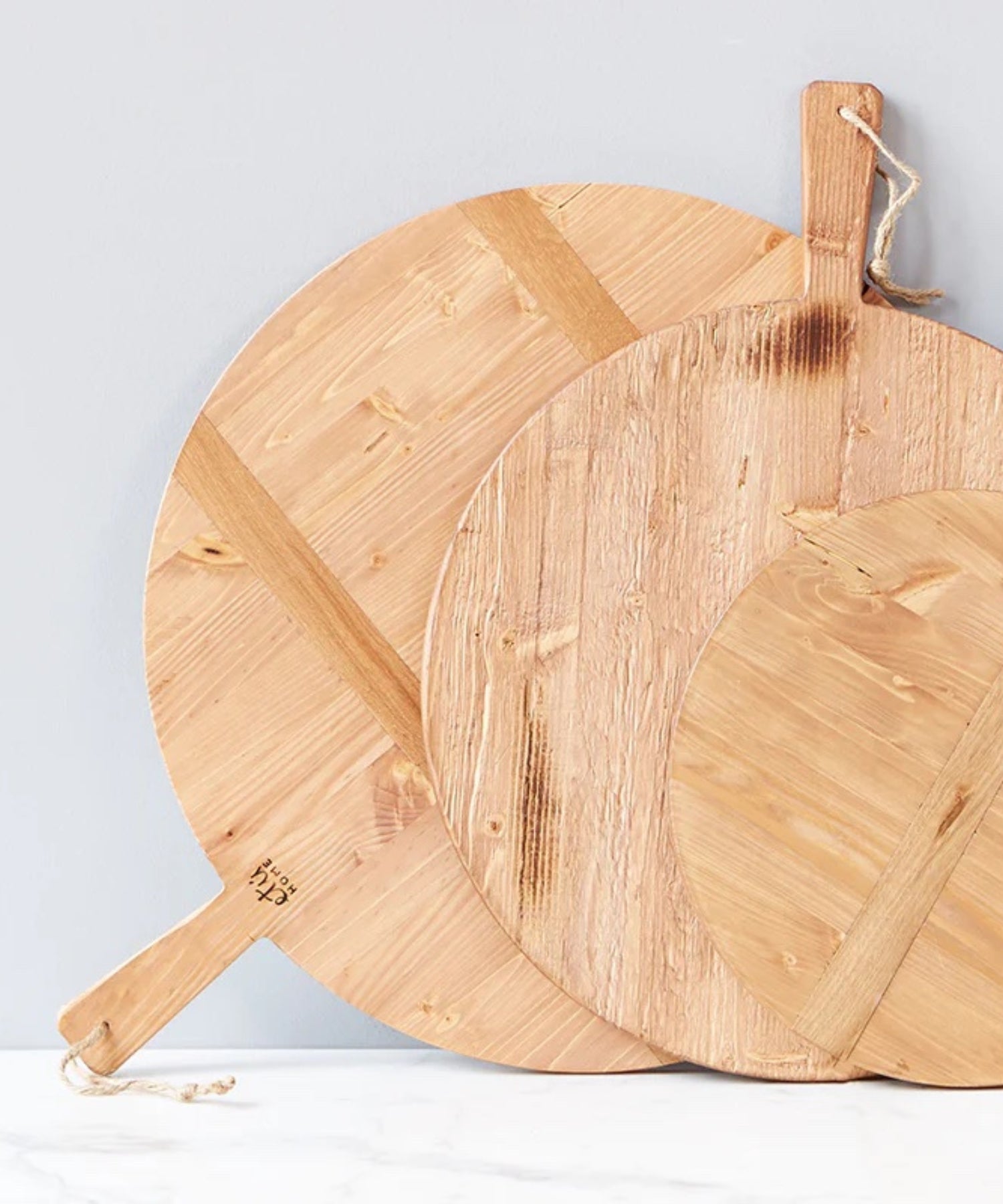 Three round pine wood cutting boards in various sizes with a smooth surface and natural grain. It has a handle with a rope loop for hanging, conveying a rustic charm.