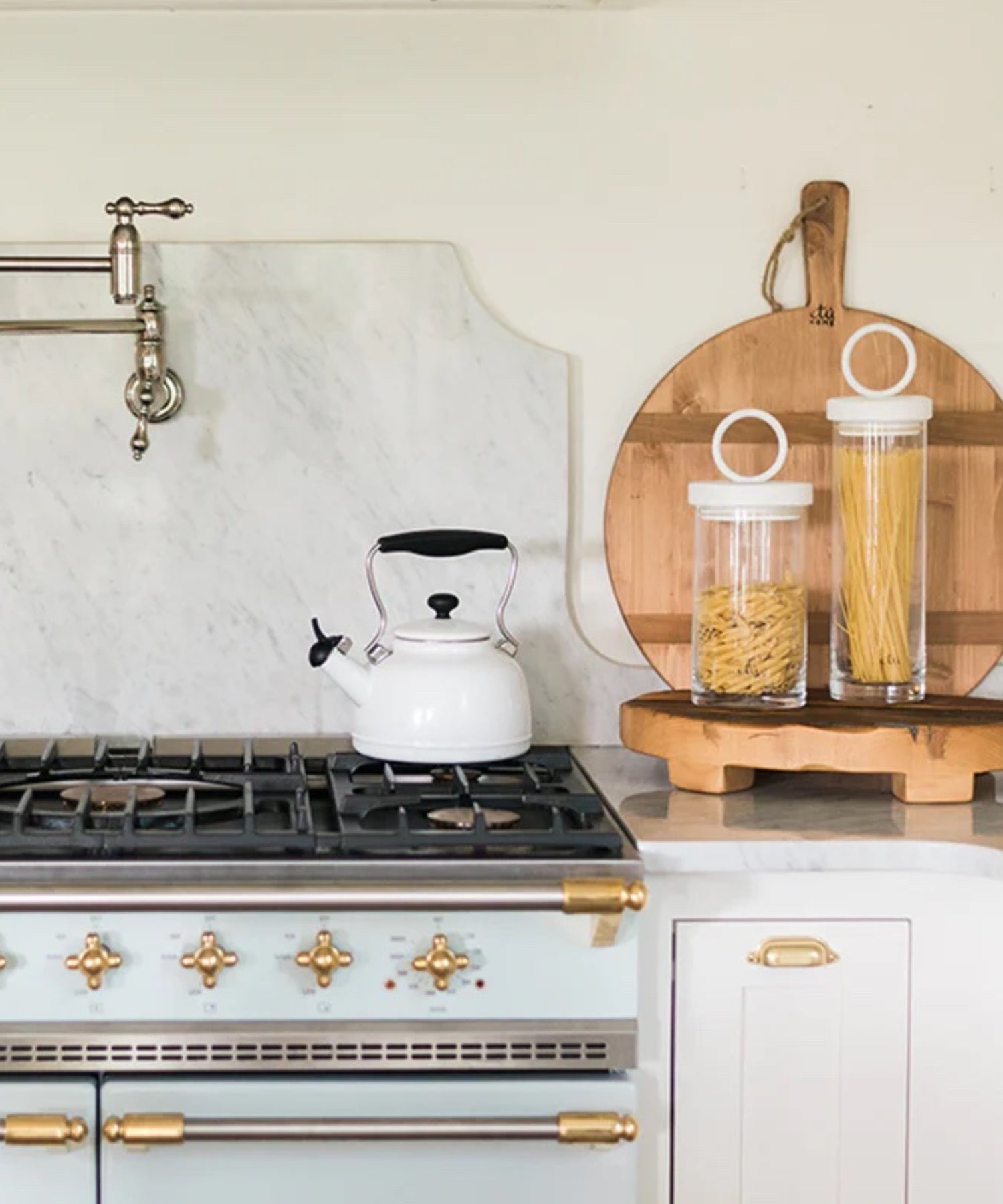 A round a wood cutting board with a smooth surface and natural grain. It has a handle with a rope loop for hanging, conveying a rustic charm styled on the counter in a neutral kitchen.