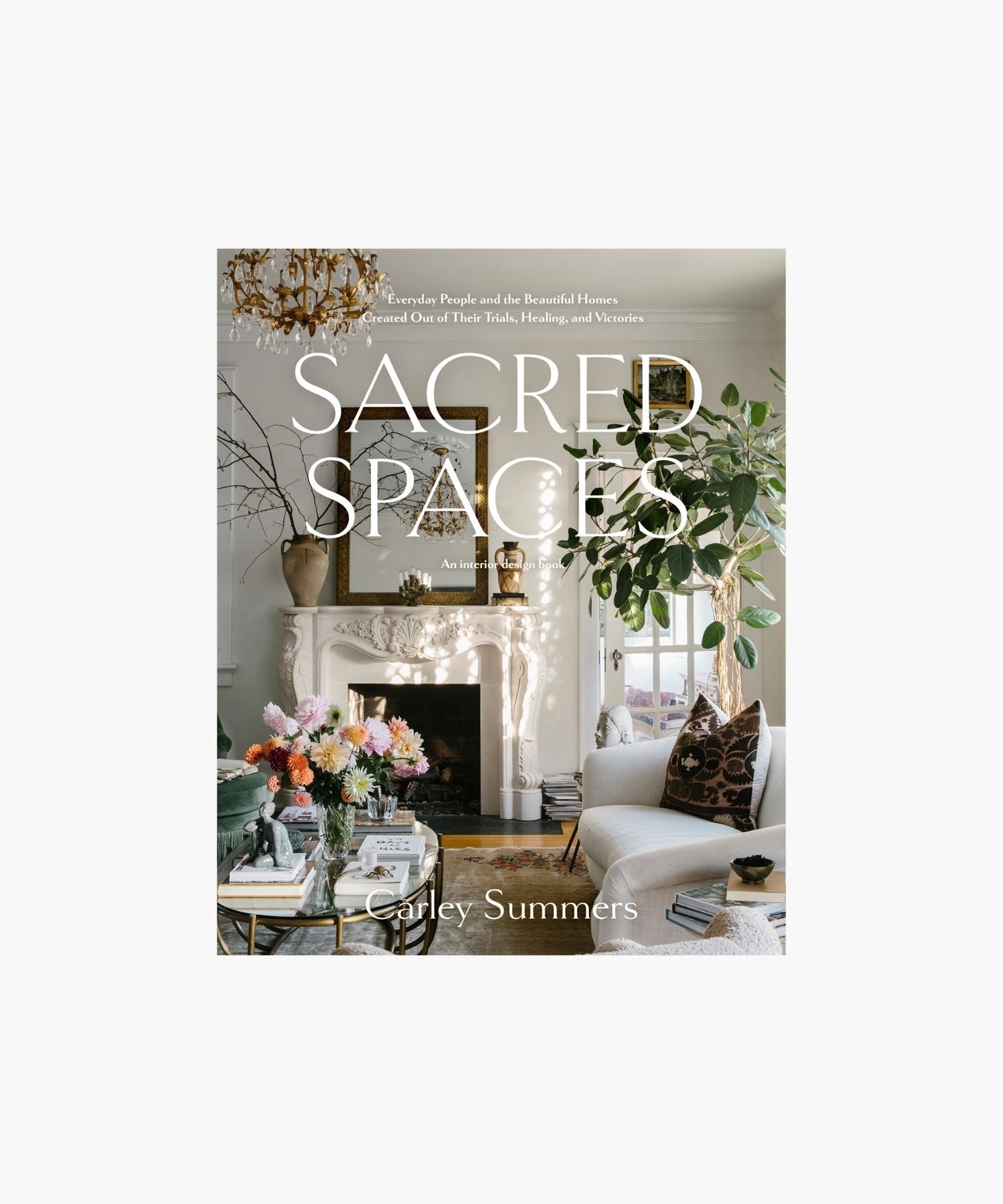 The cover of the book "Sacred Spaces" by Carley Summers featuring a cozy living room with elegant decor; a white fireplace, chandelier, vibrant flowers, and lush greenery create a tranquil, inviting ambiance.