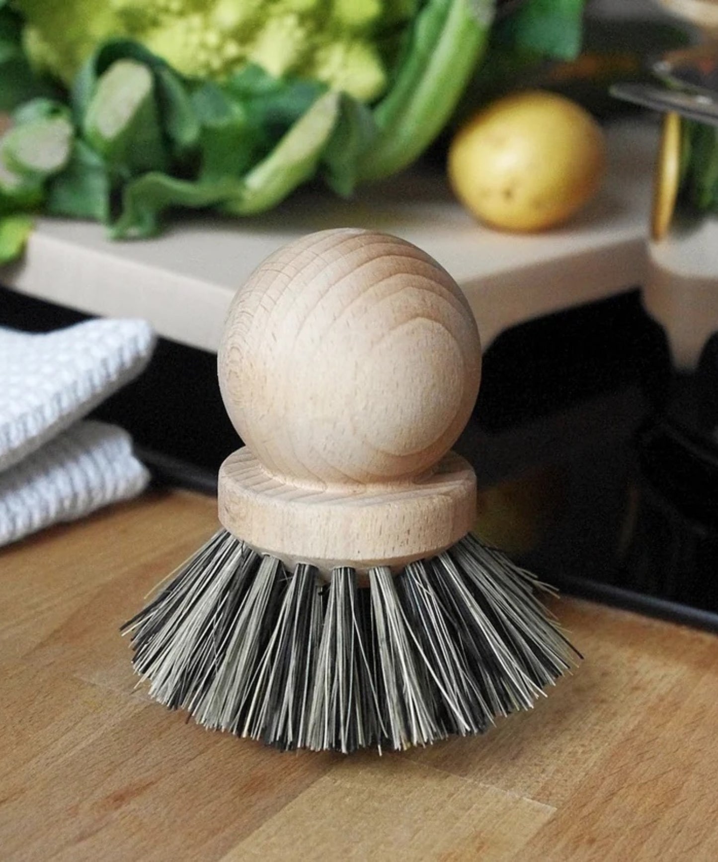 Wooden dish scrubber or saucepan brush with natural bristles, circular handle on top styled in a kitchen with neutral tones. Simple, eco-friendly cleaning tool with a minimalistic vibe.