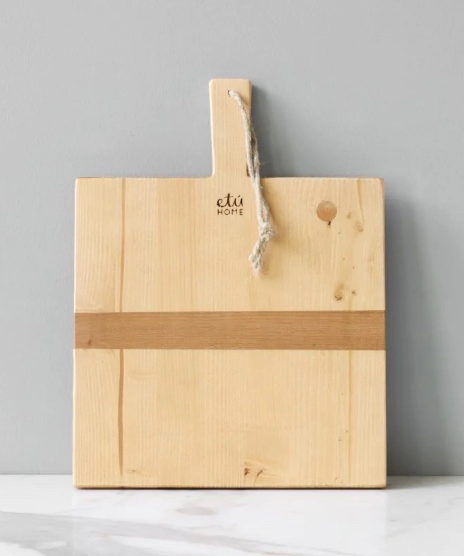 Square pine wood cutting or charcuterie board with a natural finish, featuring a dark horizontal stripe and a handle with a rope loop styled with cheese and wine. 