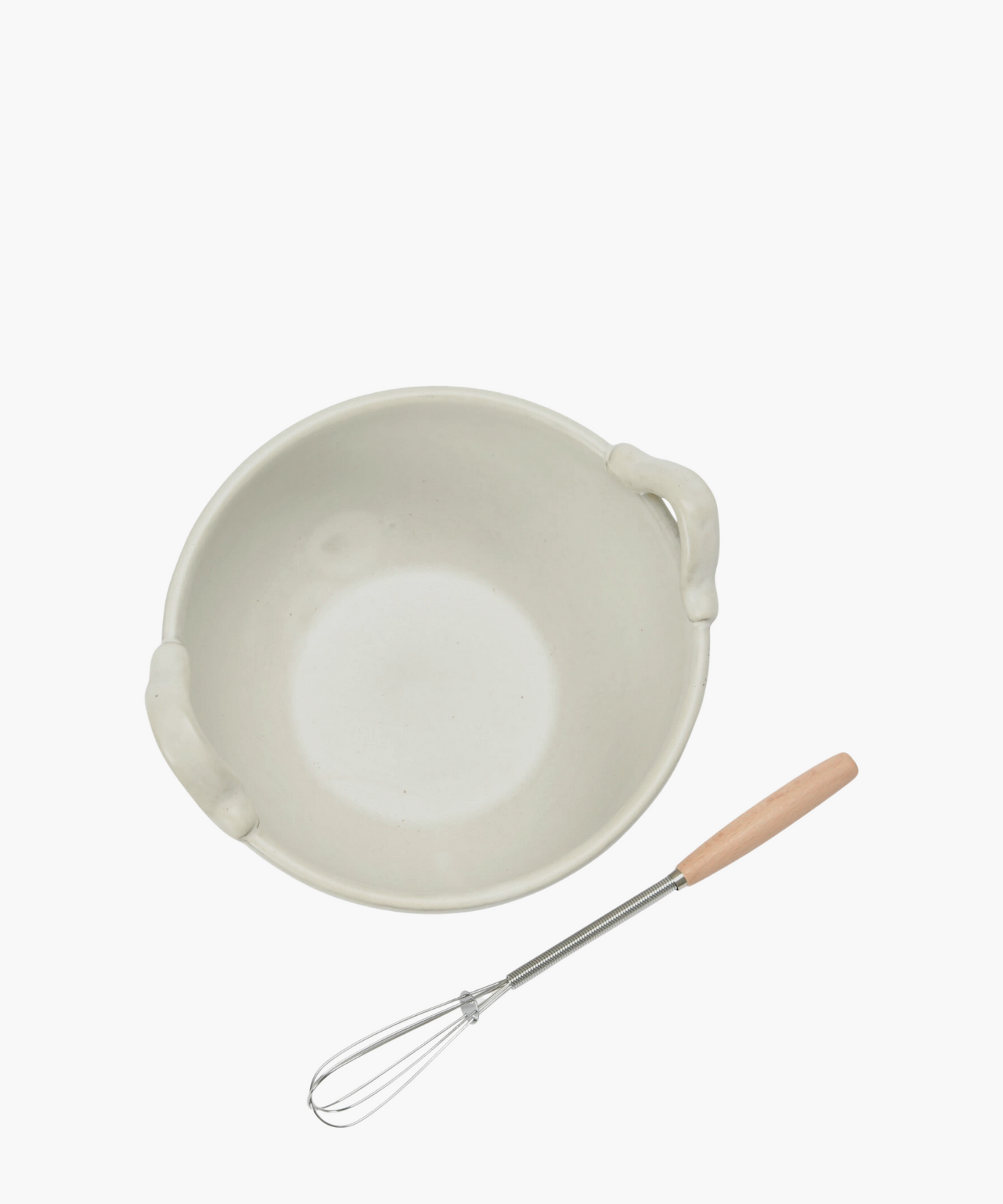 Overhead view of a cream colored stoneware ceramic mixing bowl with a metal whisk, evoking a clean, minimalist aesthetic.