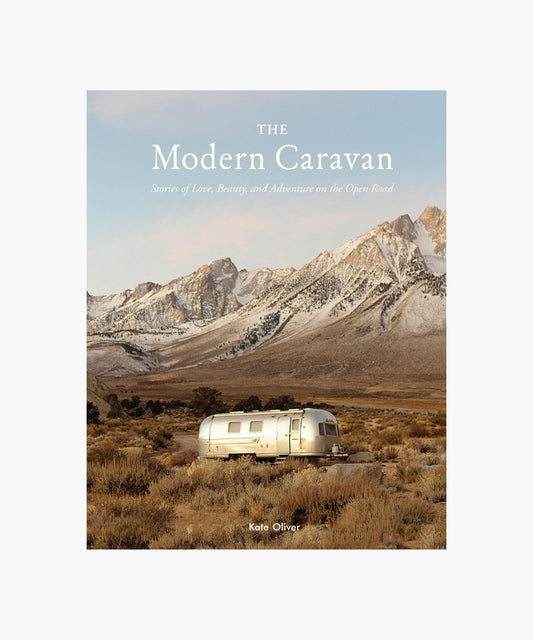 The cover of the book "The Modern Caravan" by Kate Oliver featuring a shiny silver RV in a vast, desolate landscape with rugged mountains in the background, conveying adventure.