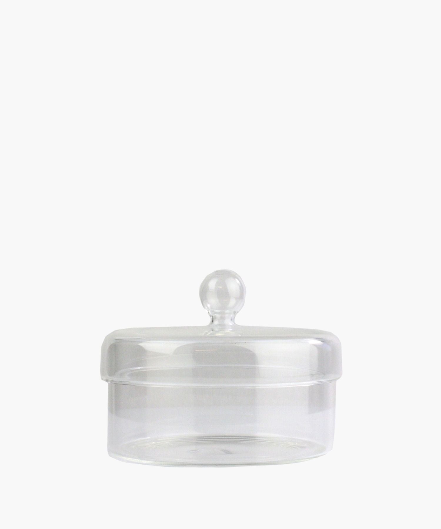 A clear glass jar with a round lid and a knob handle is centered on a plain white background. The jar is empty, conveying simplicity and elegance.