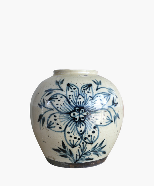 A cream toned vintage vase features a large, intricate blue floral design with leaves. The style is traditional, conveying a rustic and artistic feel.