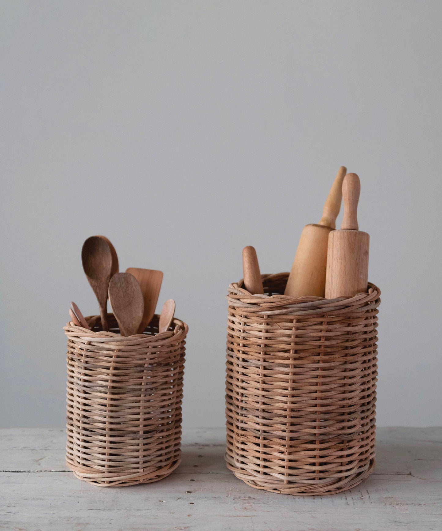 Hand woven wicker basket container in 2 sizes styled with wooden spoons and rolling pins. Both have a natural, woven texture, evoking a rustic, cozy feel.