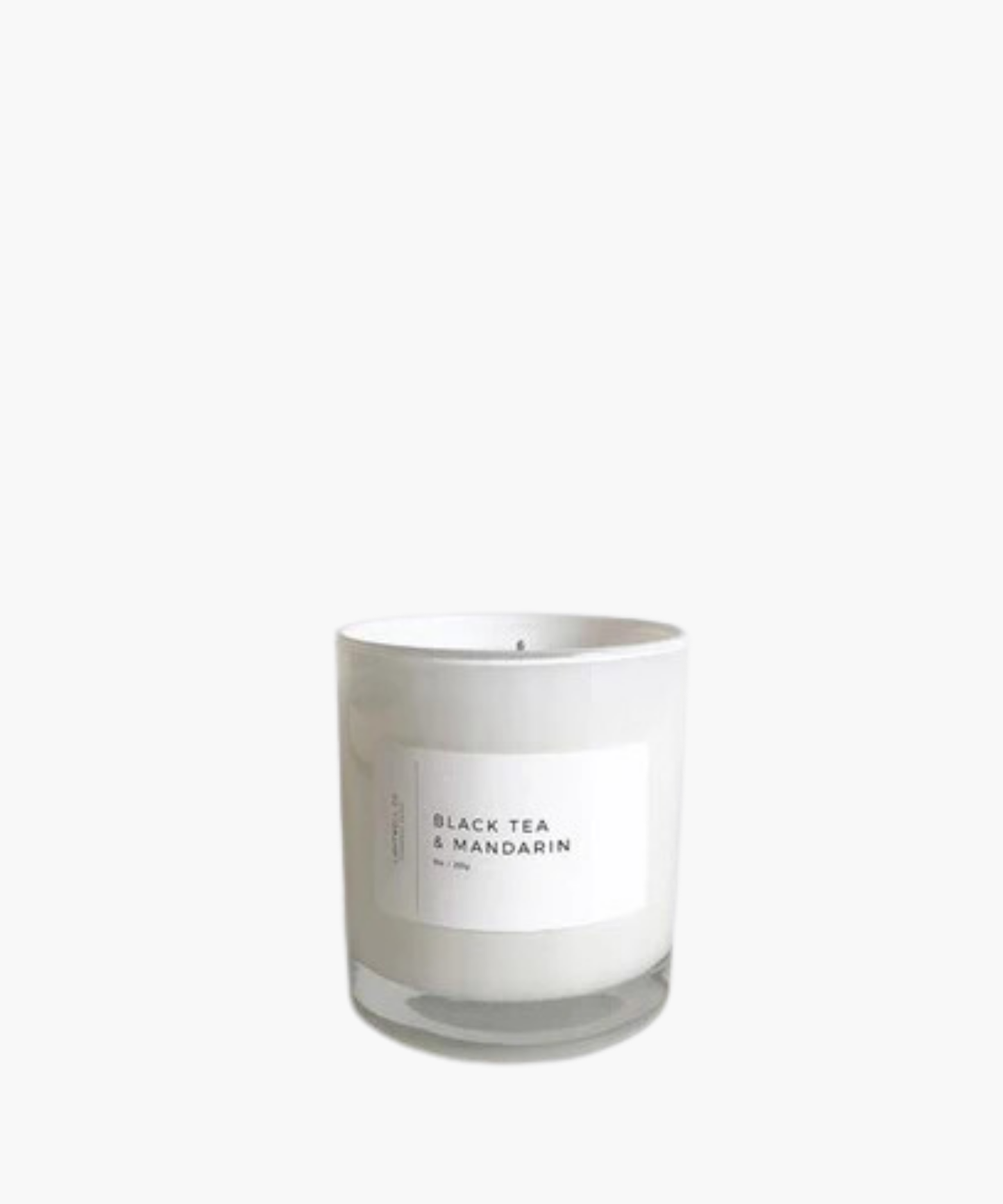 A white candle in a glass jar with a minimalist label reading "Black Tea & Mandarin." The design conveys a clean, calming aesthetic.