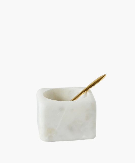 A white marble square salt cellar with a smooth finish and a small, elegant golden spoon resting inside, conveying a sense of luxury and simplicity.