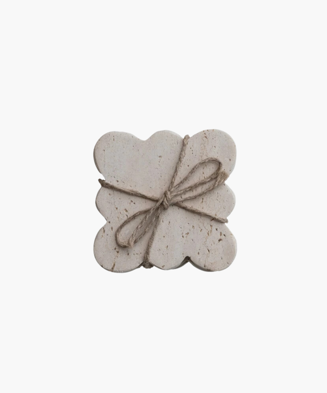 Travertine rectangular coasters with scalloped edges, wrapped in rustic twine tied in a bow. The coasters have a natural, textured appearance, evoking simplicity.