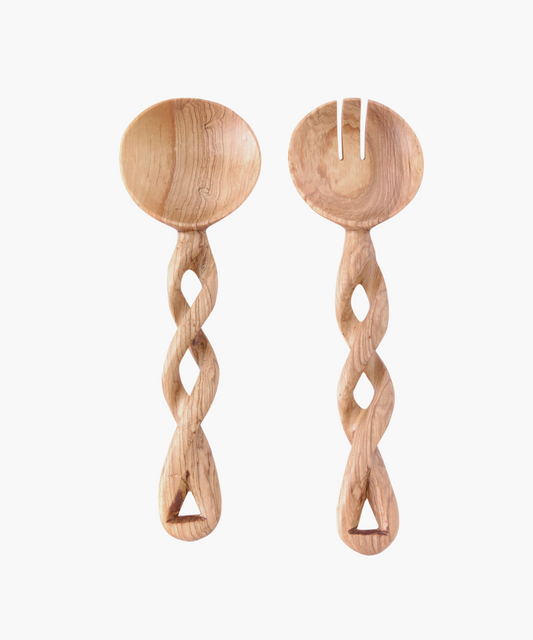 Two intricately carved wooden salad servers with twisted handles on a white background. One is a spoon, the other a fork. Warm, rustic tone.